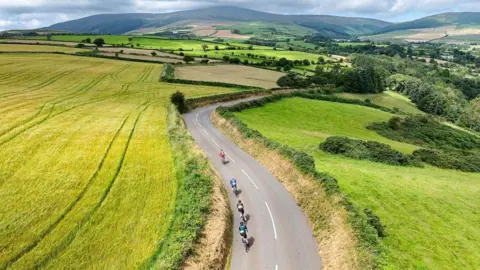 Gran Fondo Isle of Man An aerial shot of four riders cycle on a road in the countryside.