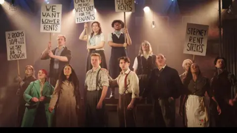 Cast hold banners dressed in 1930's clothes.