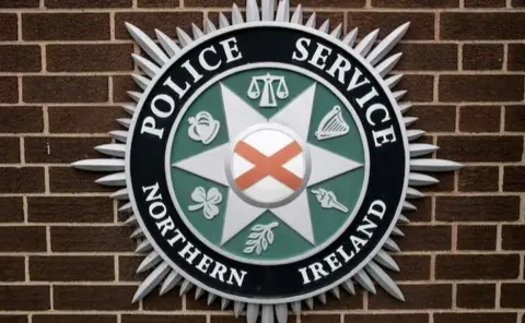A police service Northern Ireland crest on a red brick wall