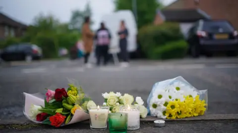 PA Media Cellophane-wrapped flowers and candles on the road where the attack happened