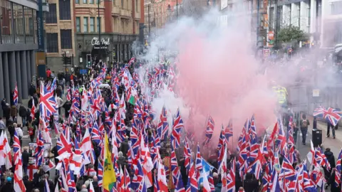 Reuters Hundreds of Union flags are held aloft with a red smoke flare rising above as Britain First protestors pack out part of Oxford Street with high-rise buildings on either side.