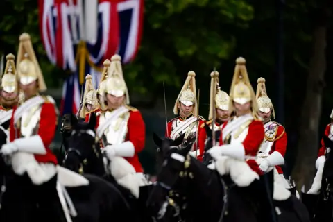 PA Media Horseback military personnel wearing red uniforms and gold headwear march down the Mall.