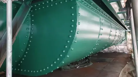 Newcastle City Council Close-up view of a restored section of the Tyne Bridge showing scaffolding and the structure's heavily riveted lower west arch, freshly painted in the shade Hollybush Green.