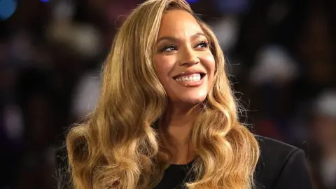 Beyonce Knowles, an African-American woman with shoulder length brown hair, smiles broadly