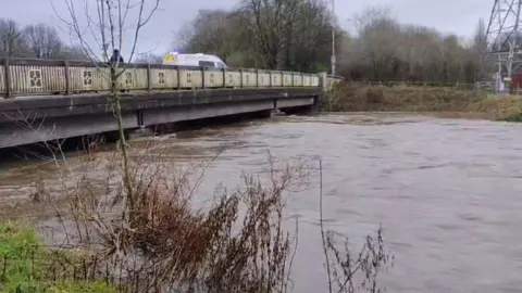 Stewart Whittingham/BBC Very high flood water close to the bottom of a bridge crossing the river. A police van is parked on the bridge