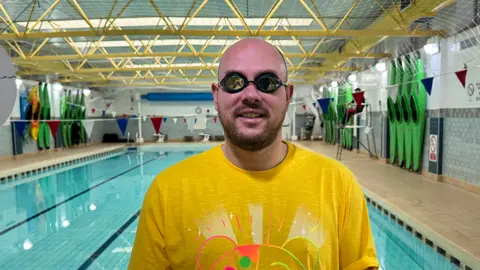 BBC Radio Shropshire presenter Mark Elliott standing at the edge of a pool, wearing goggles and a yellow Pudsey t-shirt