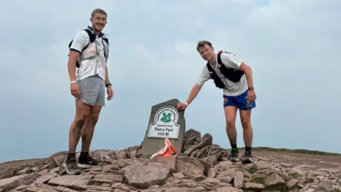 Two male runners in white shirts and blue shorts at the top of Pen y Fan