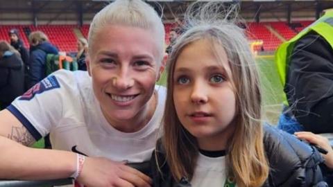 Beth England with short blond hair and Caitlin Passey with long brown hair at a football stadium