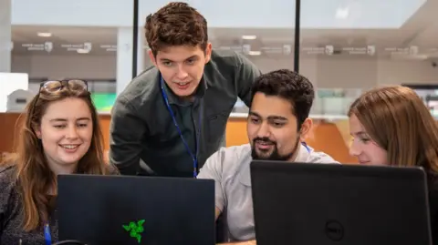 Harper Adams University Four students, two men and two women, study at a pair of laptops in a glass-fronted room at the centre. 