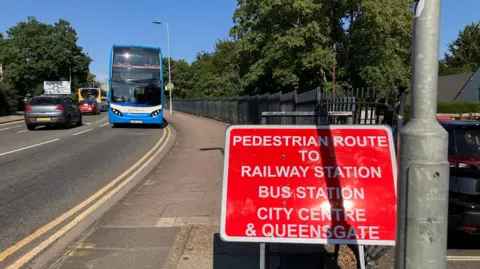 Shariqua Ahmed/BBC A red and white signboard placed on the footpath.