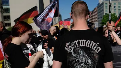 Young neo-Nazis with German flags, including one young man with a black t-shirt that reads: "Germania", wait to be allowed by police to resume a demonstration in Berlin last year.