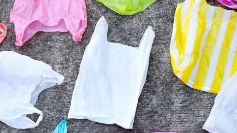 Getty Images A handful of colourful plastic carrier bags flattened and laid neatly upon a grey floor. 