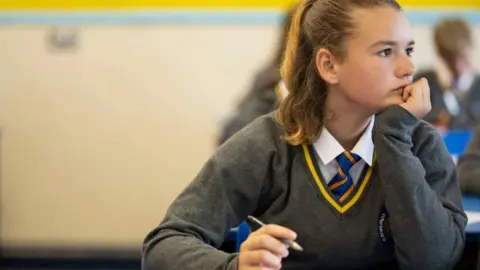 Getty Images A pupil listens during a history lesson at Whitchurch High School on September 14, 2021 in Cardiff, Wales. The teenager is wearing a grey jumper, with a white shirt and blue and orange striped tie. 