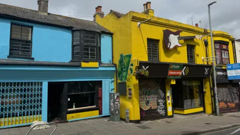 A yellow building is in the process of being painted blue 
