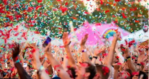 A picture of the crowd cheering as rainbow confetti falls.
