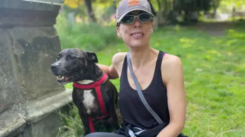 Claire Rafferty  wearing hat and sunglasses with dog at a gravestone