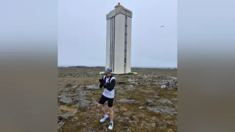 Jack Pitcher stood in front of an obelisk in northern Ireland, ready to start his challenge. The weather is grey behind him.