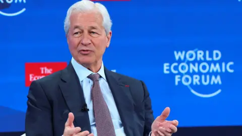 The CEO of JPMorgan Chase, Jamie Dimon, in a navy blue suit speaks in front of a blue World Economic Forum (WEF) backdrop at the conference in Davos, Switzerland, January 21, 2026