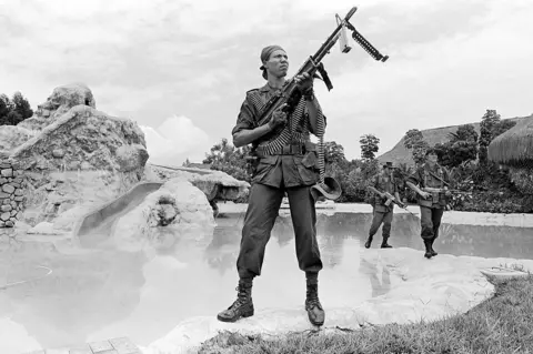 Getty Images In a black and white photograph soldiers carry heavy weapons are they search a compound.