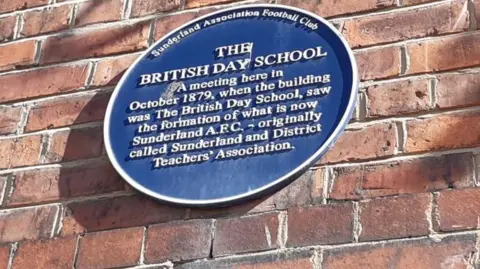 A round blue plaque on a brick wall saying it used to be the British Day School and a meeting was held in October 1879, where the formation of what is now Sunderland AFC took place.