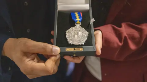 Birmingham City University Two people hold a silver medal which lies in a black box.