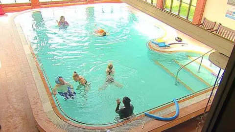 People swimming in a hydrotherapy pool. Its windows overlook marine lake in Southport.