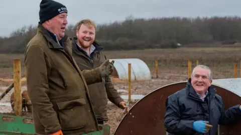 Amazon MGM Studios Jeremy Clarkson, farm manager Kaleb Cooper and vet Dilwyn Evans all smiling near pig pens on Clarkson's farm 