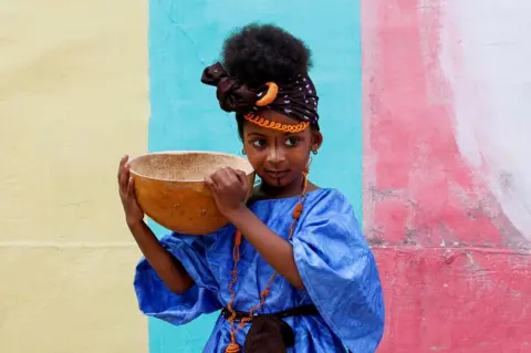 Luc Gnago / Reuters A girl wears a blue dress and carries a calabash.