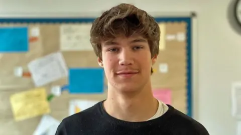 Branwen Jefferies / BBC Charlie smiles on camera, with a colorful noticeboard on the class wall behind it