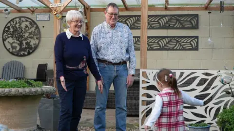 North Yorkshire Council Margaret and Ted Metcalfe playing in their garden with a foster child, wearing a tartan dress 