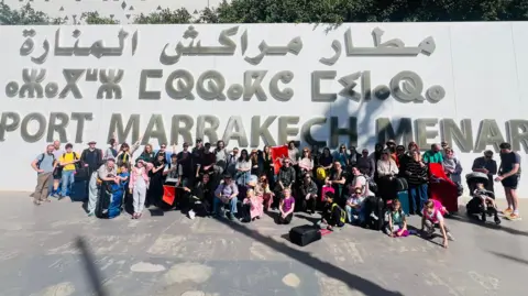 Skeddan Jiarg The group in casual clothes sitting in a group in front of a wall with the word Marrakech visible behind them.