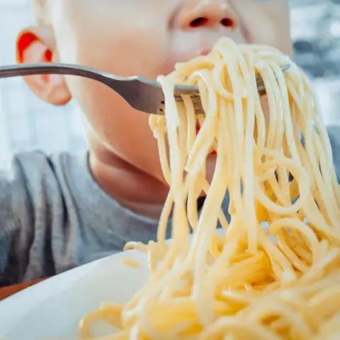 Getty Images Young child eating spaghetti in a kitchen