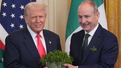 PA Media Trump is wearing a dark blazer, white shirt and pink tie. Martin also as a white shirt on but a green tie. His breast pocket is stuffed with shamrock.