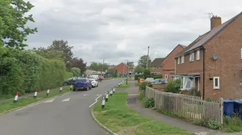 A residential road with semi-detached brick houses and cars parked along the road. 