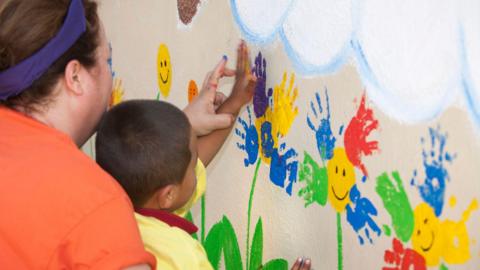 Stock photo of a nursery teacher finger painting with a child