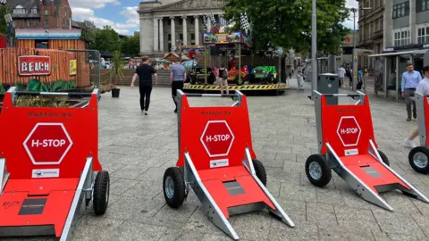 Three safety barriers with red stop signs on them in front of the entrance to the city centre beach in Nottingham