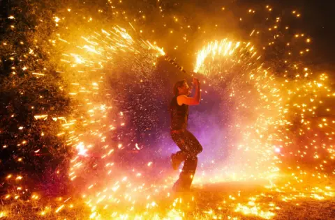 A performer sprays fire and sparks around them as they perform for the crowds at Wychwood Festival 2025