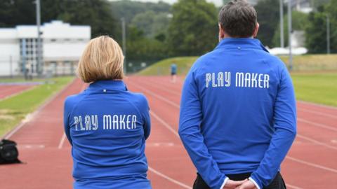 A woman and a man wearing blue jumpers that read playmaker
