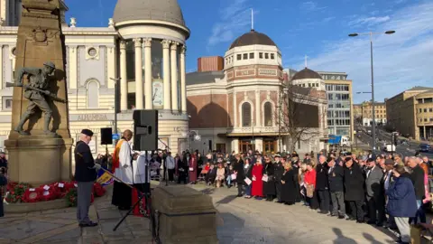 Hundreds of people, many in uniform, praying in front of Bradford war memorial. 