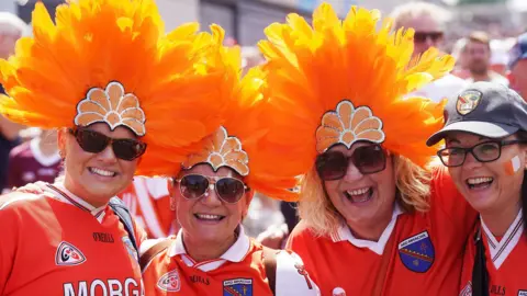 PA Three women wear bright orange feather hates. A forth is wearing a baseball cap