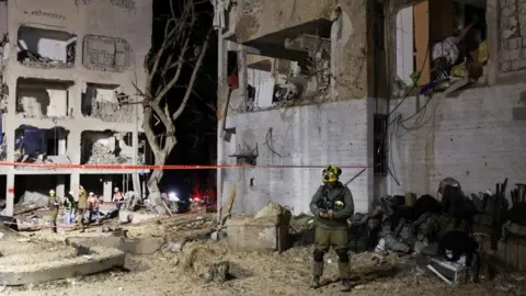 Damaged buildings and emergency workers in Arad at night after Iranian missile strike