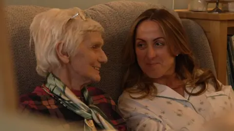 Big Mountain Productions/BBC Natalie chatting with Poppy Lodge resident Monica, sat on a sofa