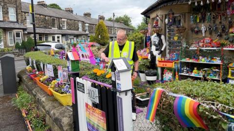 Paul dressed in a hi-vis jacket tends to some of the hundreds of toys in his garden which is strewn with Pride flags