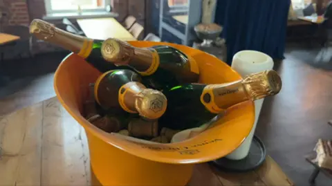 An ice bucket filled with mini champagne bottles sits on a wooden table in the Pumproom restaurant.