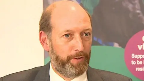 BBC Bill Borrett is pictured mid-interview looking away from the camera. He is bald with a light coloured and grey beard. 