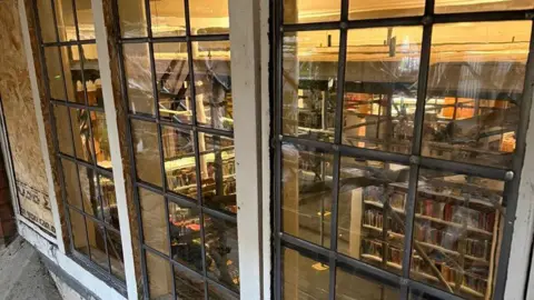 North Northamptonshire Council Stained glass windows, with a library behind them. There are several panes of glass, with metal round each pane. 