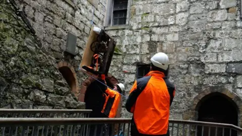 MNH Workmen guiding the clock as it is lowered