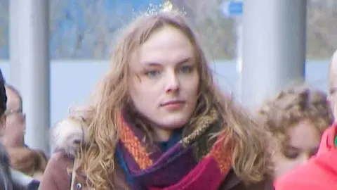 Dr Beth Upton has long brown hair and wears a colourful scarf and a brown parka jacket.