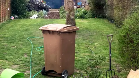 A brown wheelie bin, placed on the grass in the garden. 