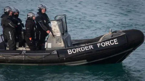 PA Media Border Force officials in black wet gear are pictured in a black small boat in the English Channel